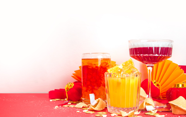 Three different colored mocktails garnished with fruit on a red table.