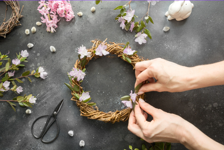 Person attaching fake flowers to a wreath made out of twigs